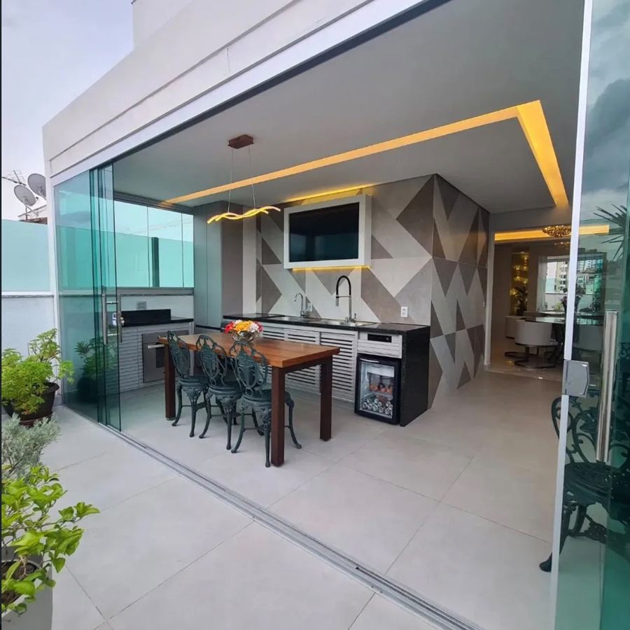 Área gourmet envidraçada com bancada, churrasqueira e mesa de madeira