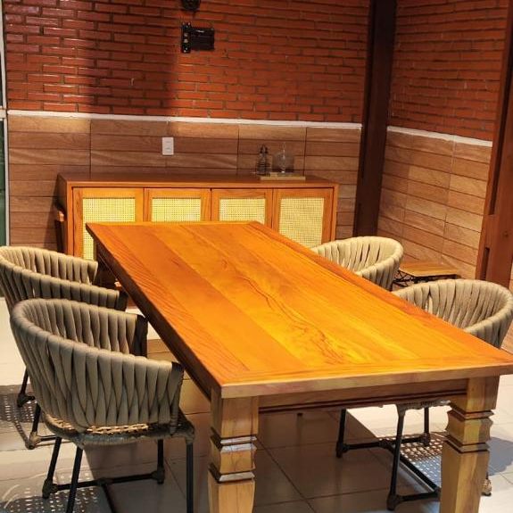 Varanda gourmet com parede de tijolinho e mesa de madeira maciça